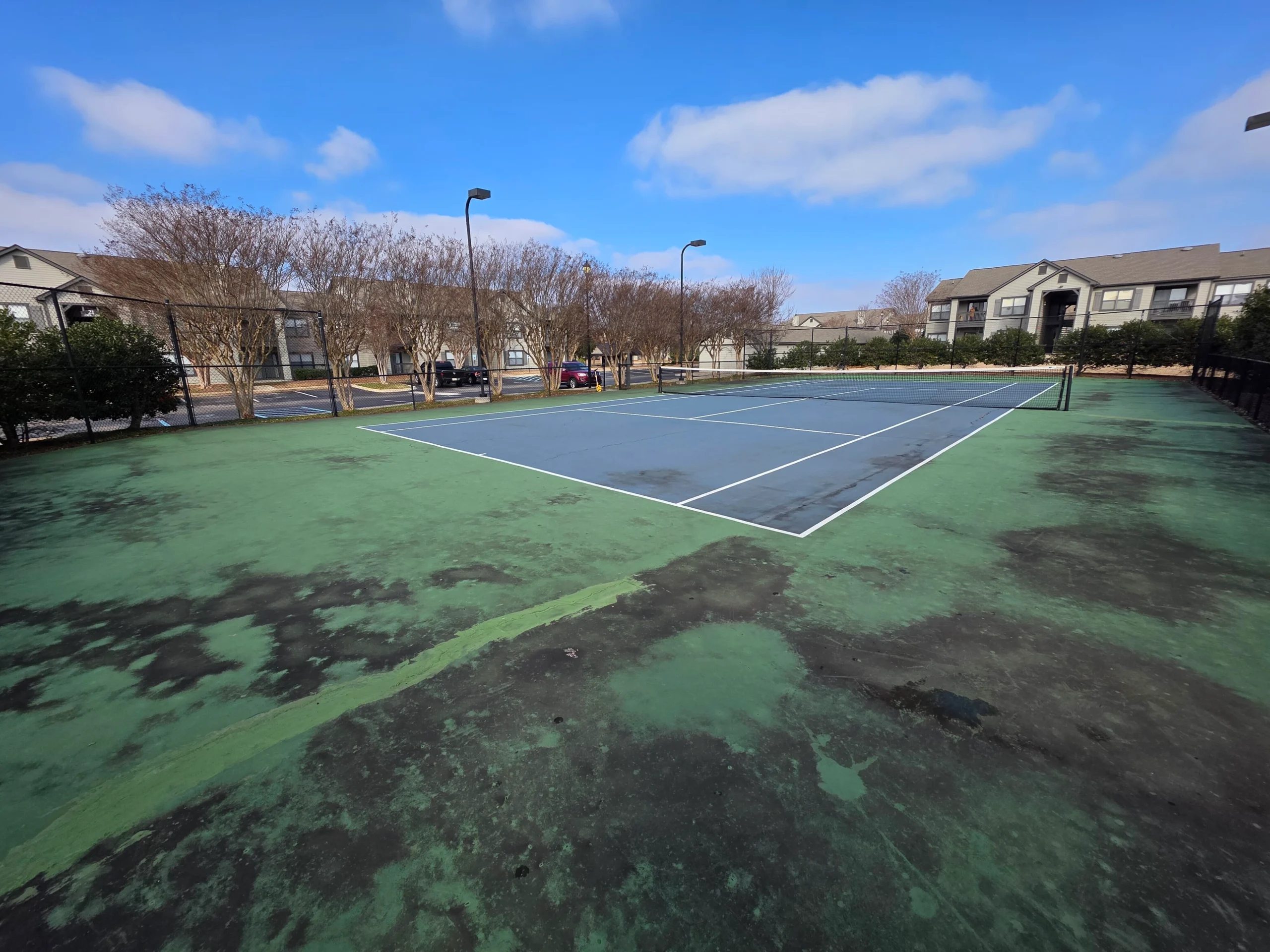 Worn apartment tennis court with stained surface before resurfacing at Weston Ranch in Madison, AL