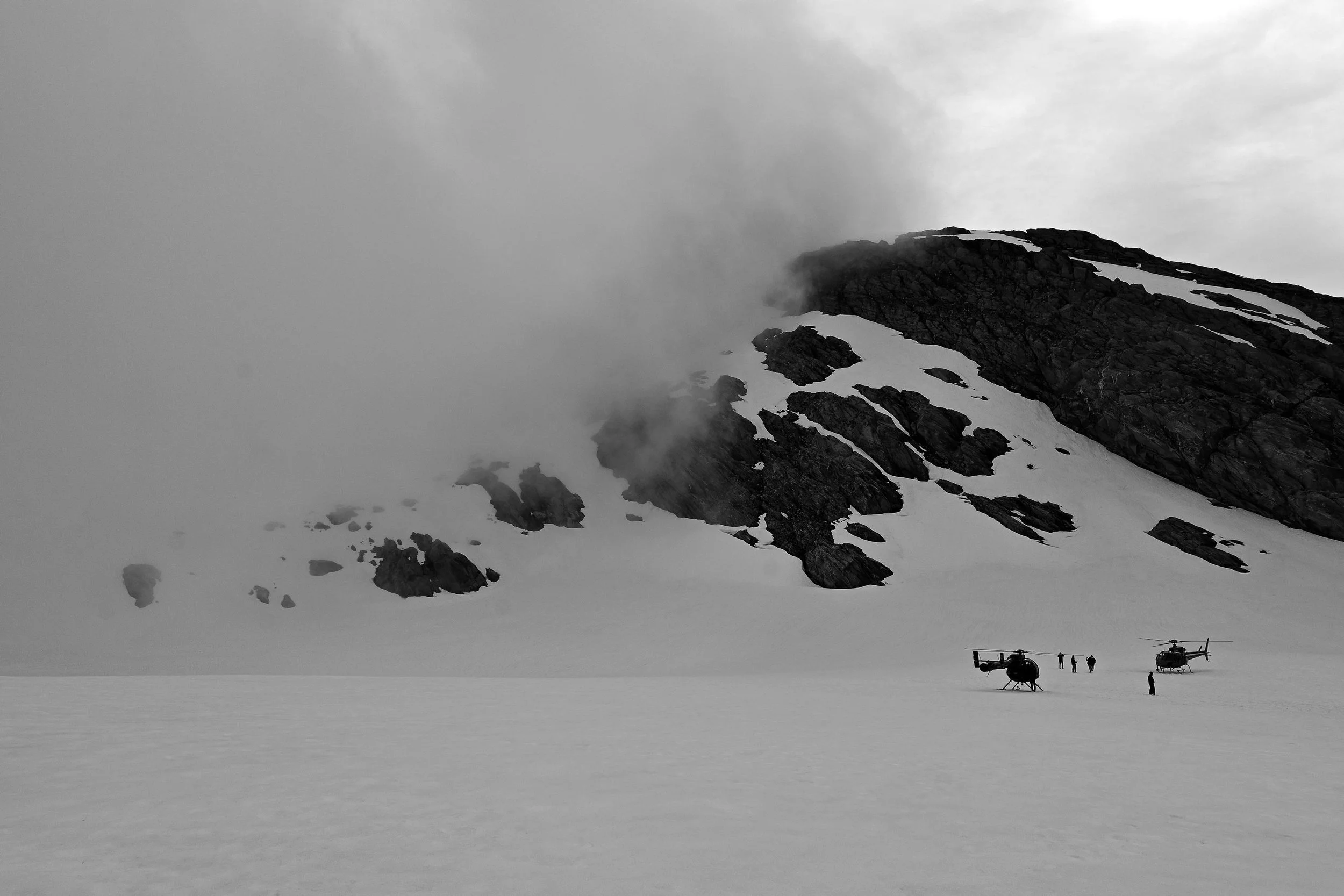 A steep snow-covered mountain cliff face with mist