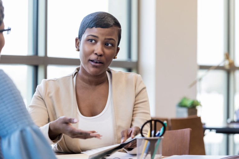 A woman in a professional setting holding a tablet and engaged in conversation, representing new staff induction and onboarding for nurses, carers and support workers in care homes