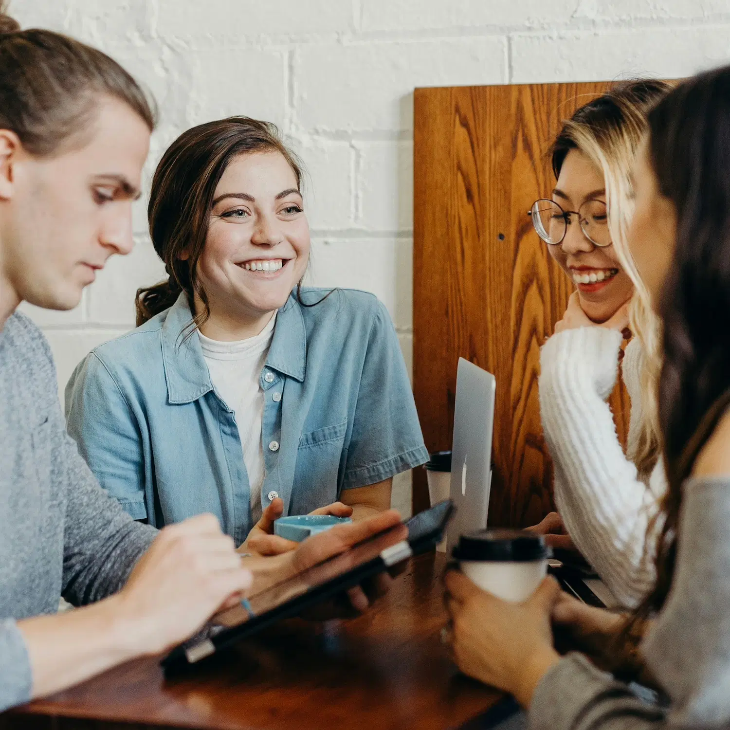 Group of young adults smiling and connecting over coffee and laptops, symbolizing supportive and affirming therapy for bisexual and pansexual individuals in NYC.