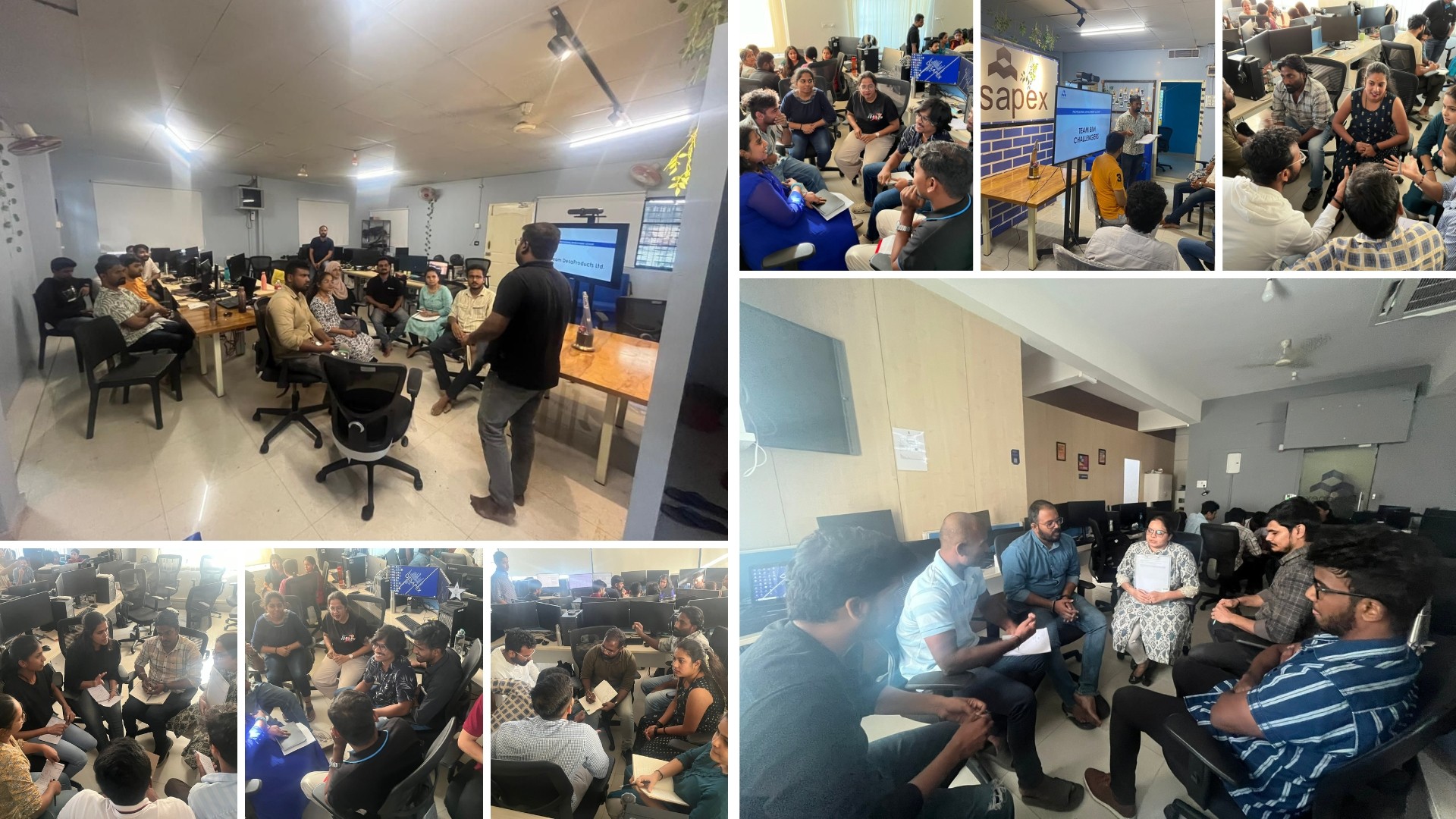 A man stands while two people sit at a table in an office setting, smiling and engaged in conversation. The mood is friendly and collaborative.