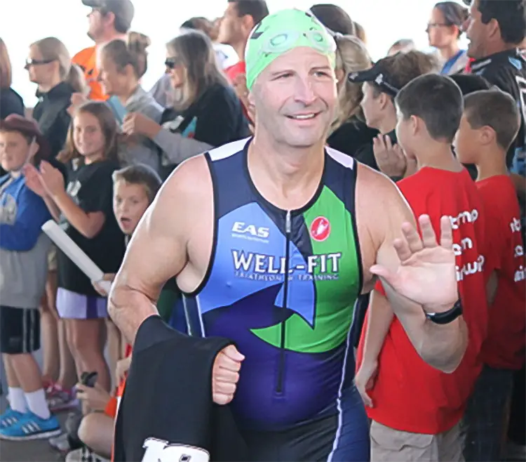 Well-Fit triathlon athlete in a green swim cap and Well-Fit tri suit waving to the crowd after the swim leg of a triathlon
