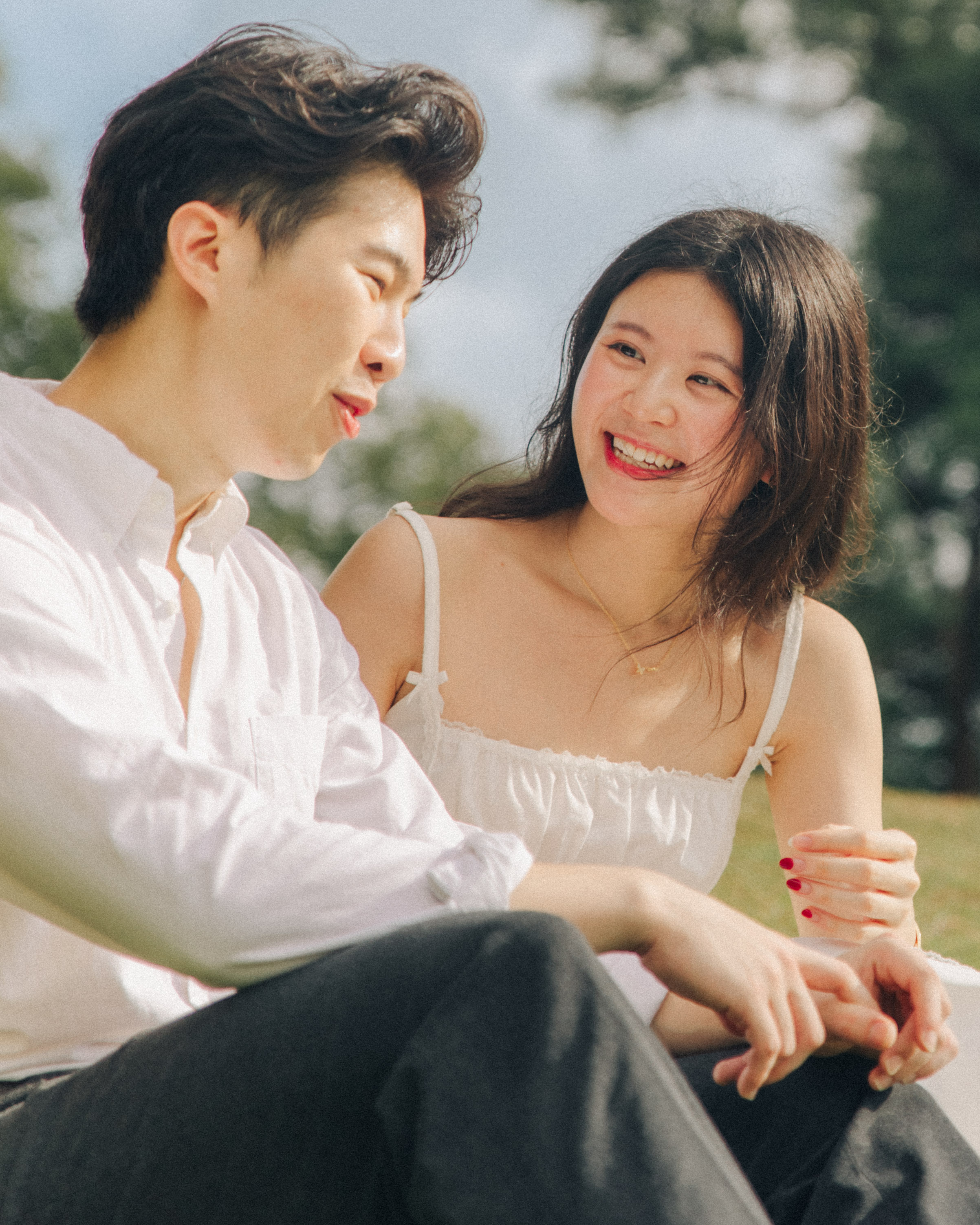 Candid moment of the graduating couple relaxing on a shady lawn area in Singapore Botanic Gardens.
