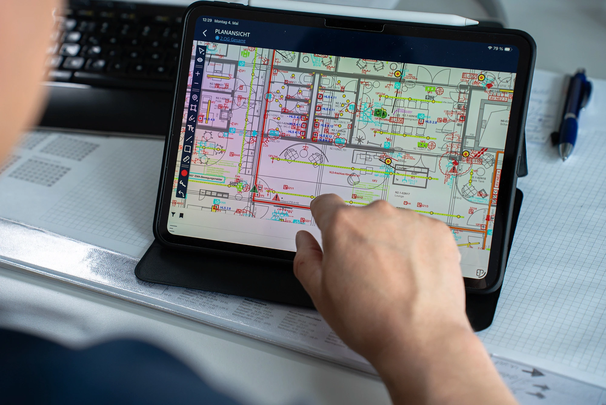 Hand zeigt auf einen digitalen TGA-Gebäudeplan auf einem Tablet. Die detaillierte Planansicht unterstützt die Projektplanung und Koordination elektrotechnischer Installationen.