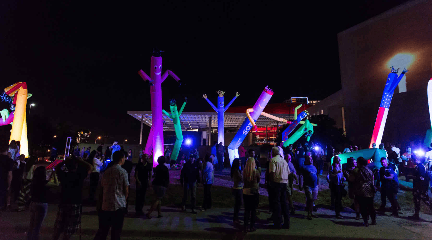 Vibrant, illuminated inflatables and colorful lights at a nighttime outdoor event with a crowd gathered.