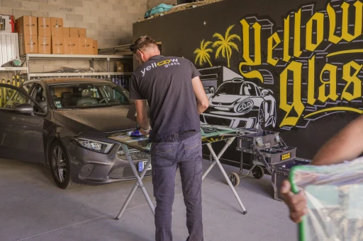Un homme répare le pare-brise d'une voiture, atelier de réparation de vitres automobiles Yellow Glas.