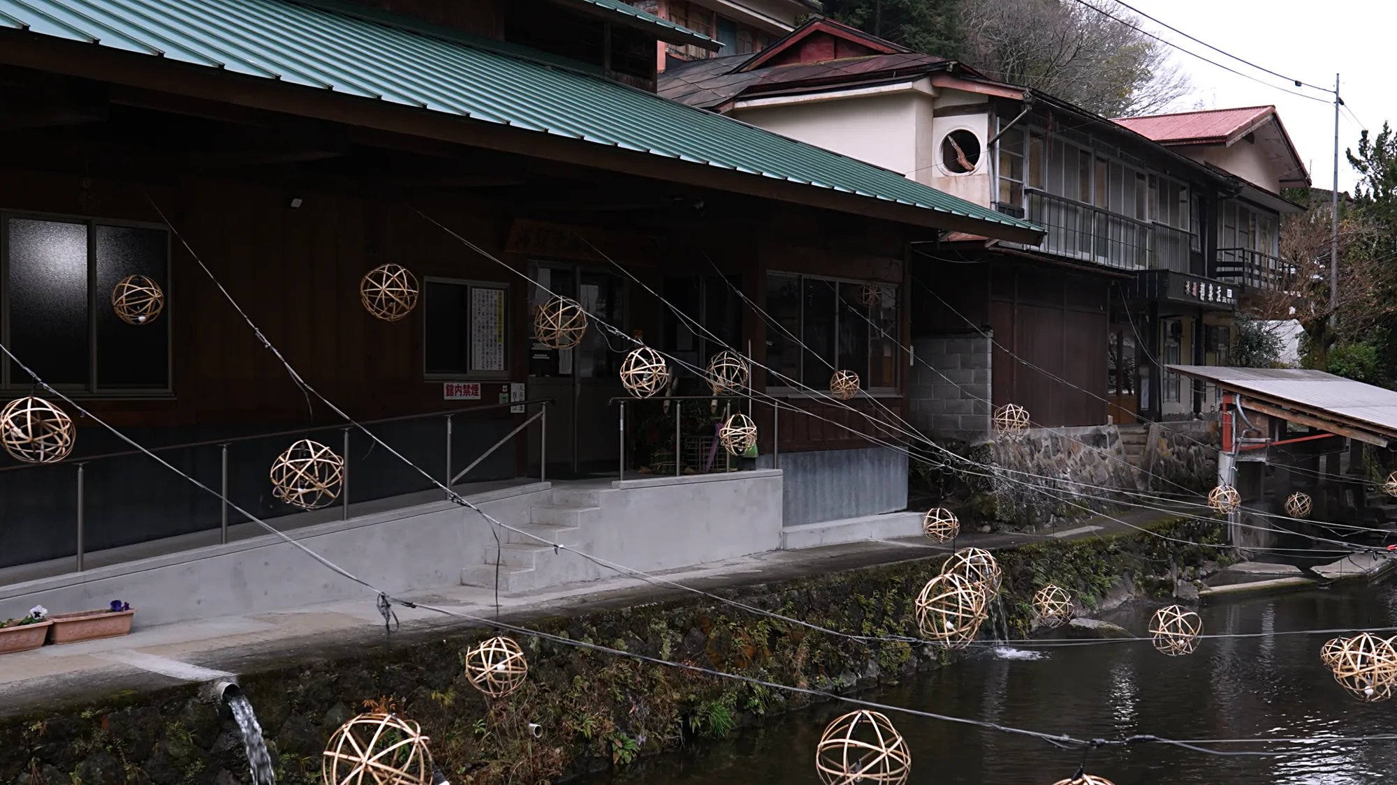 Woven-bamboo lantern spheres strung along a timber building in daylight, before Yuakari begins
