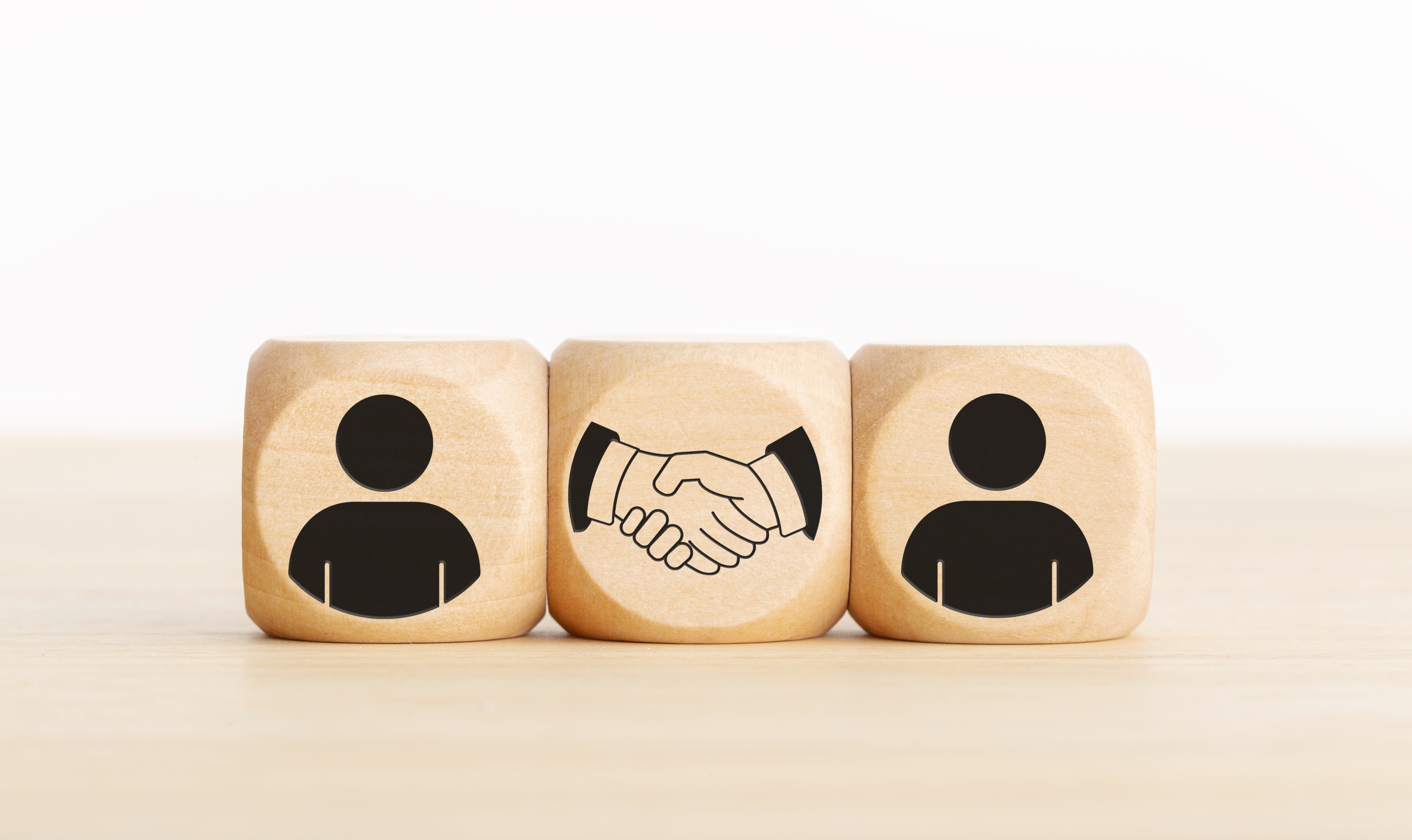 Wooden blocks displaying two user icons and a handshake icon in between, symbolizing trust, business agreement, partnership, or collaboration concept on a neutral background.
