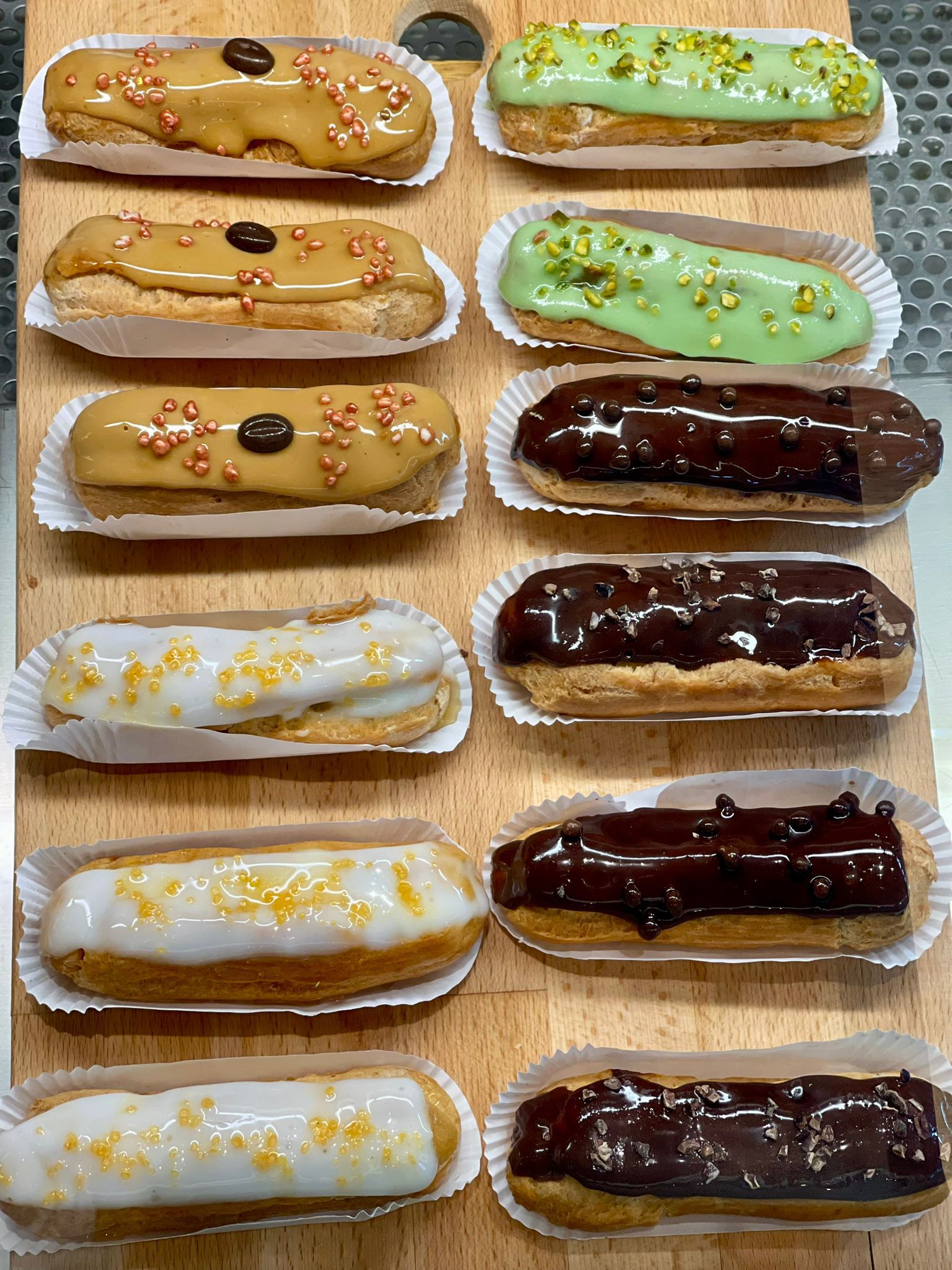 White plate with roasted carrots served on green sauce, topped with almonds and fresh herbs, held by a hand over a dark table.