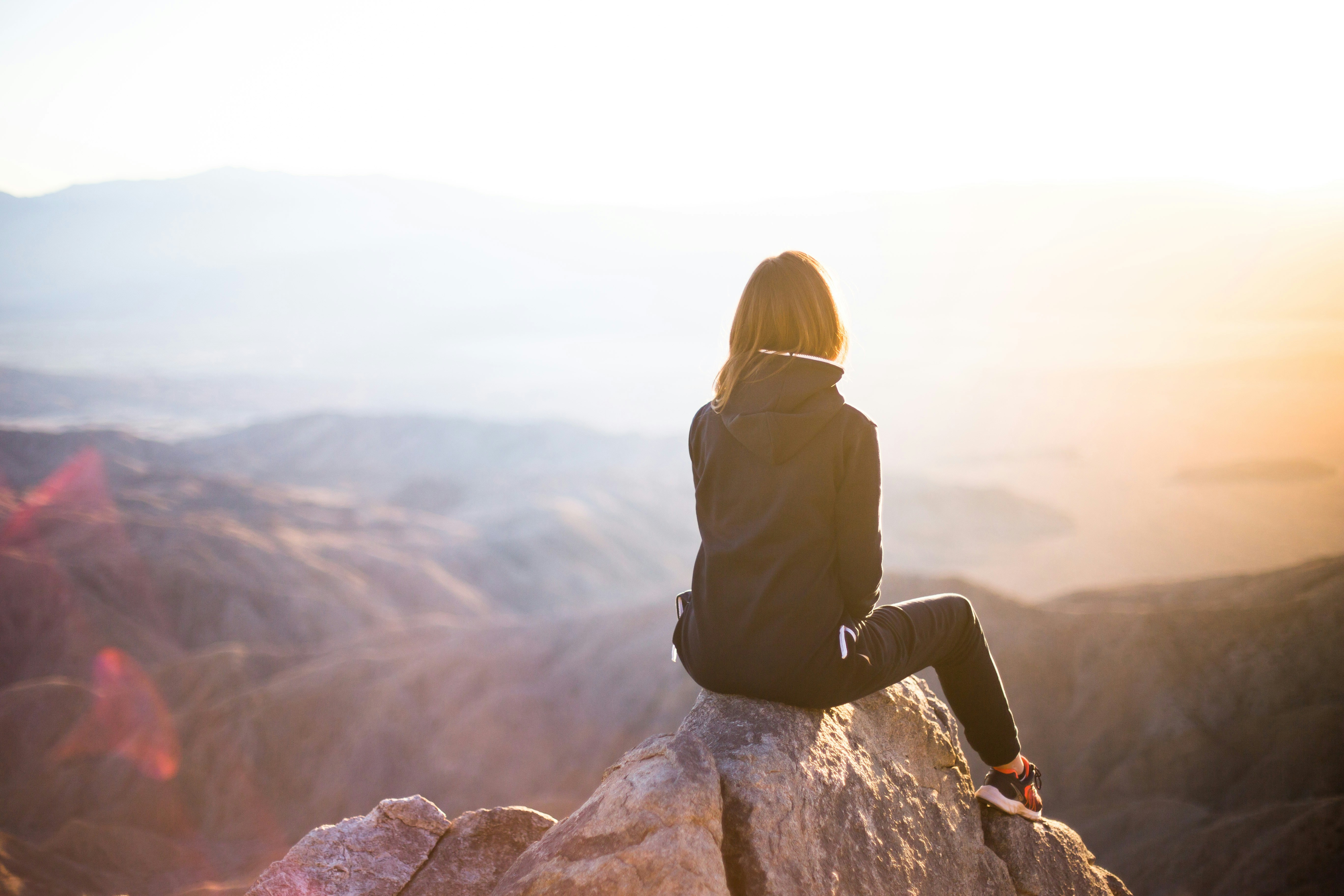 a woman sitting on a rock on a mountain watching the sunrise