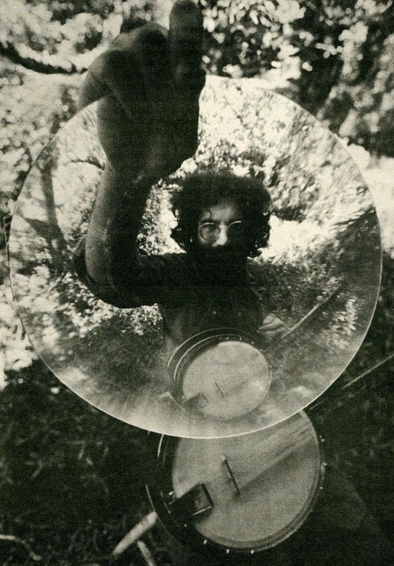 Black-and-white portrait of a bearded person seen through overlapping circular glass forms in a wooded setting.