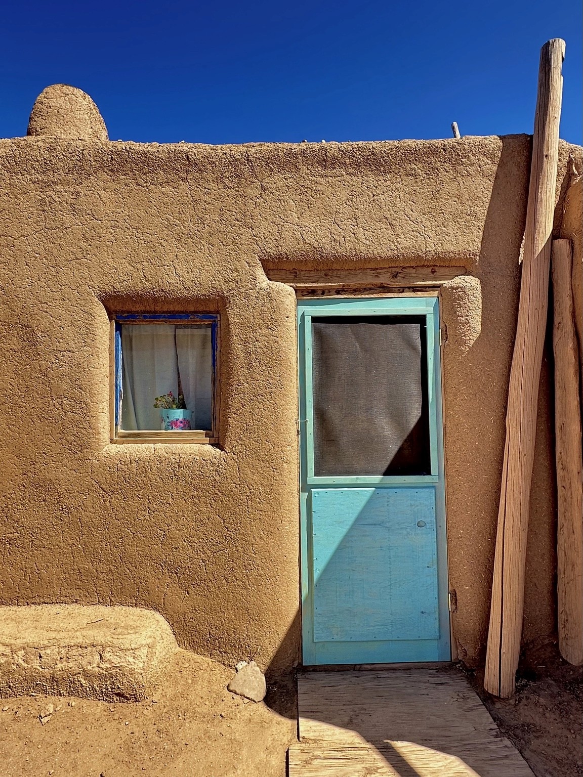 A turquoise door in warm adobe walls under a deep blue sky. Photograph by Pranjali Shah.