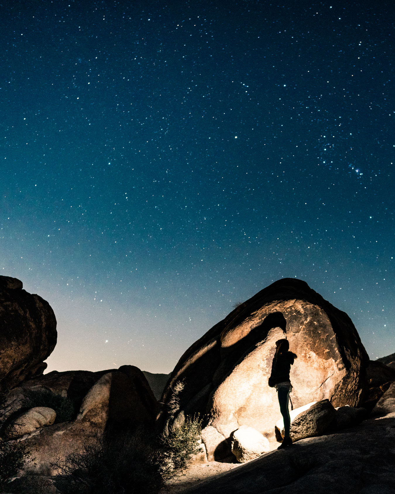 Person stood within the desert rocks under a starry sky.