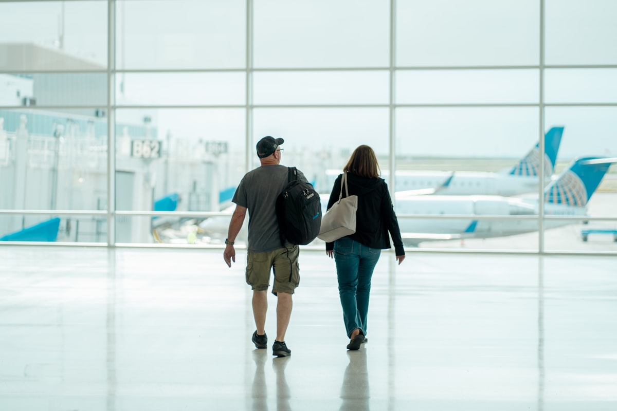 Two travelers with rolling bags walking through a bright airport terminal toward their gate