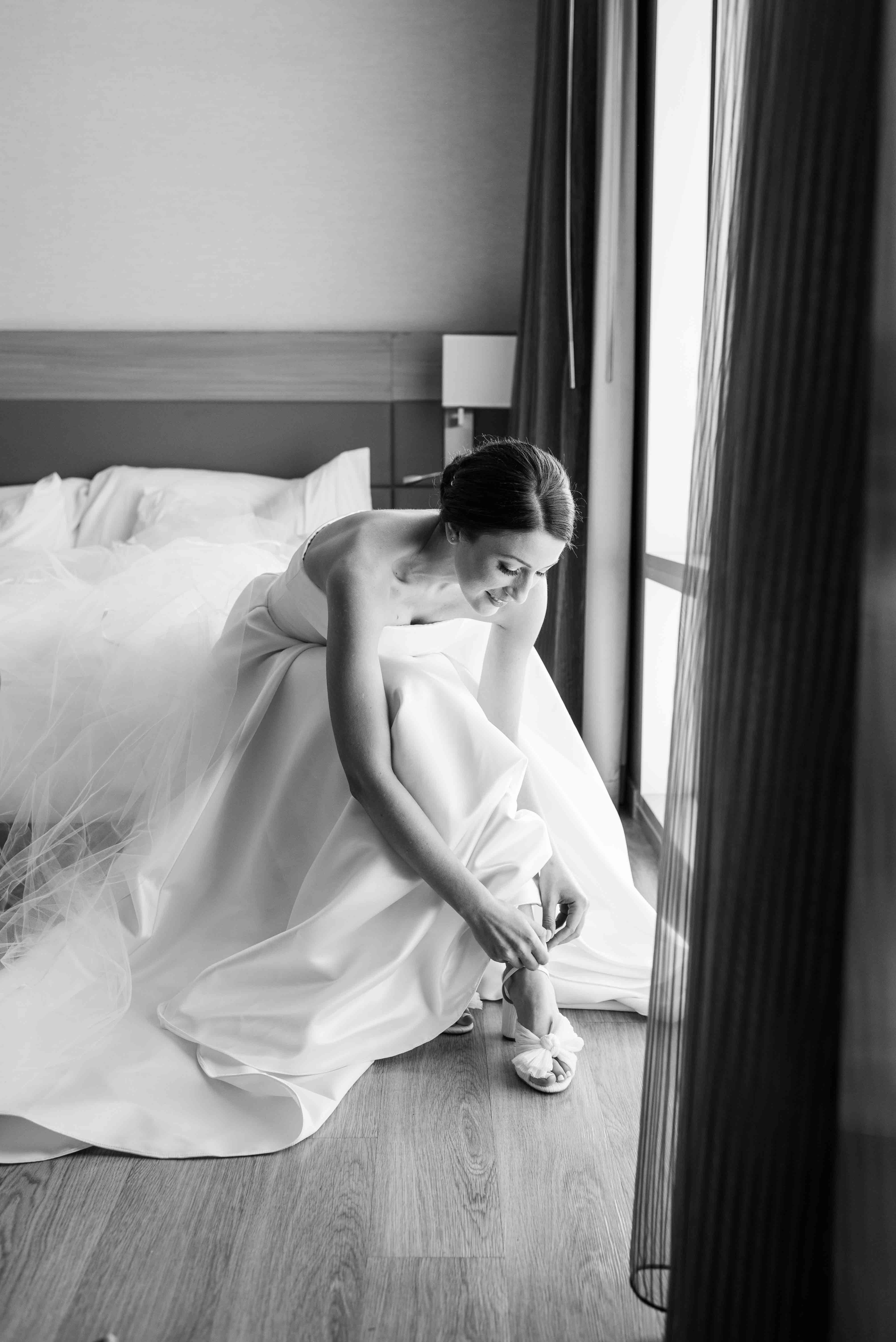 Black and white image of bride putting on her shoes.