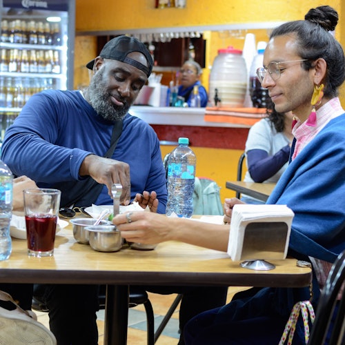 Tatlong bisita ang nakaupo sa isang kaswal na mesa sa isang lokal na taquería, nagbabahagian ng masasayang sandali habang tinatangkilik ang tradisyunal na tacos.