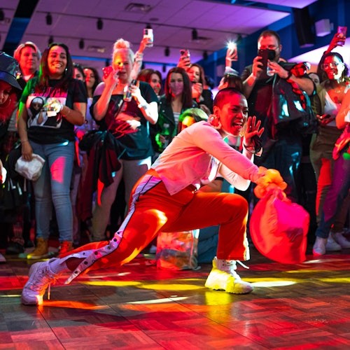 Persona bailando enérgicamente con un pañuelo en la mano, rodeada por una multitud que toma fotos y reacciona con entusiasmo.