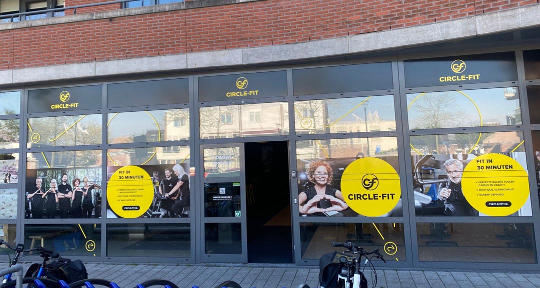 A Circle Fit with large windows featuring yellow signs and an entrance door, with customers visible inside.