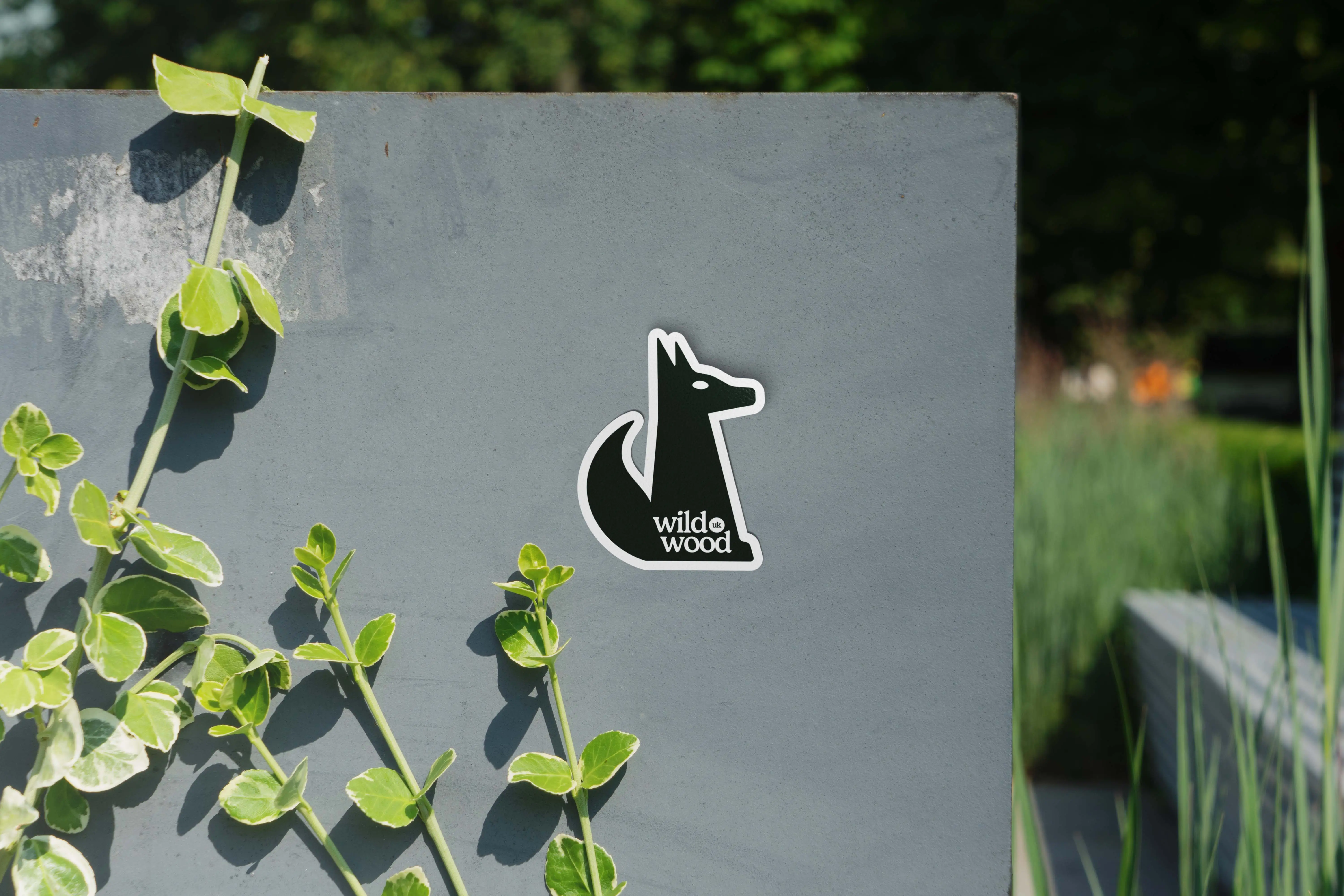 A small black and white figure is mounted on a gray wall, surrounded by green leafy vines.