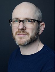 A photo of a man wearing glasses and a black t-shirt.