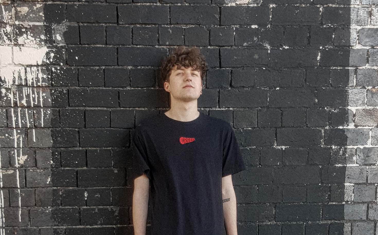 Photograph of streetwear model wearing creep branded clothing against dark brick wall.