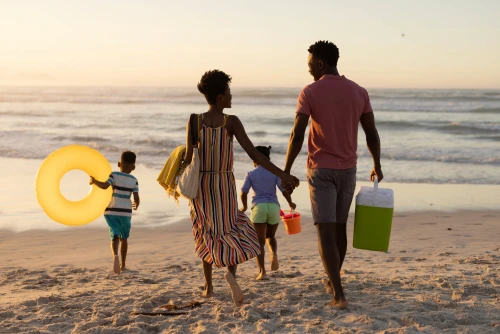 A family walking across the beach with inflatable toys and a cooler.