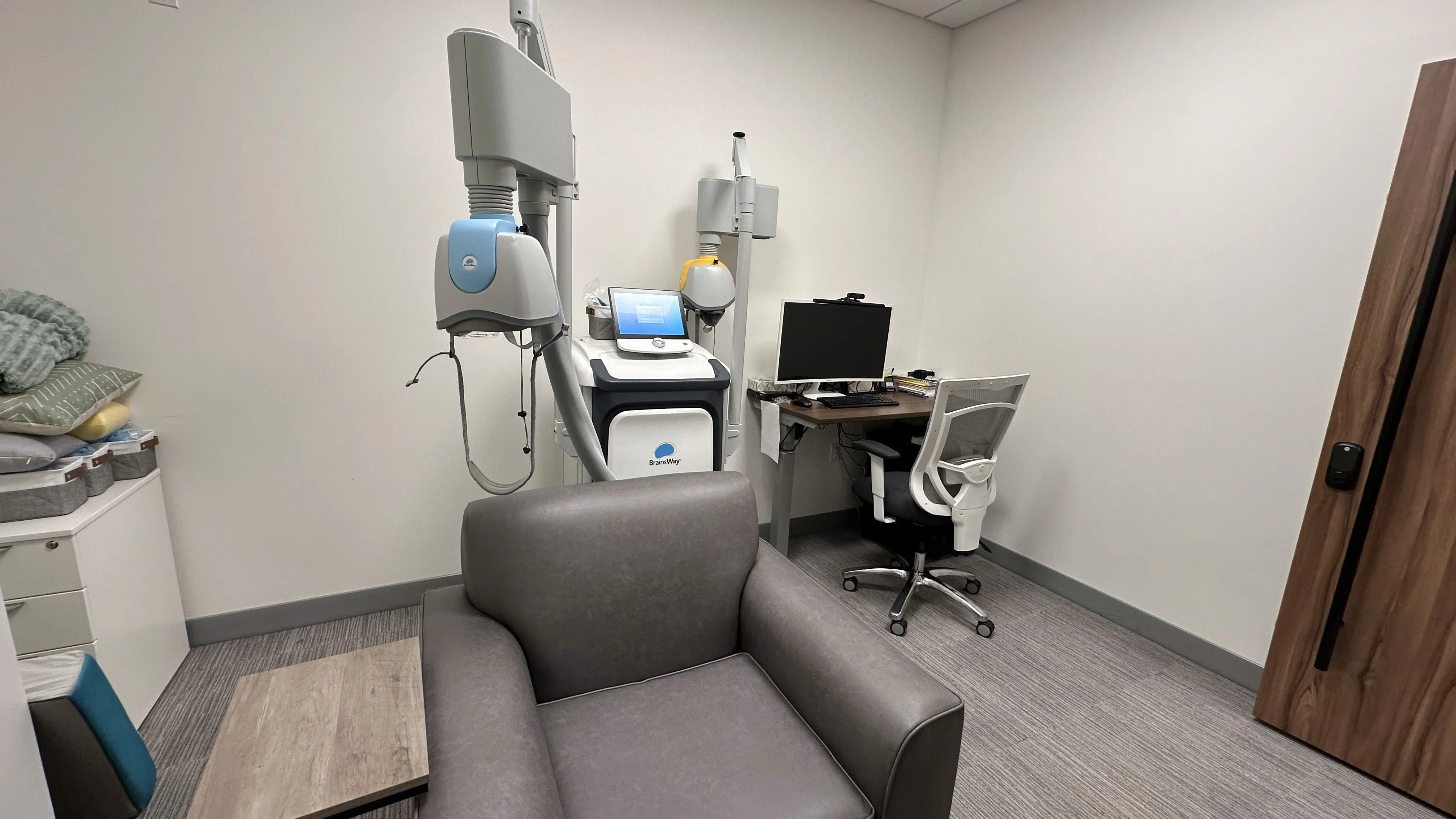 Deep TMS treatment device with coil beside a leather recliner chair and a desk with a computer