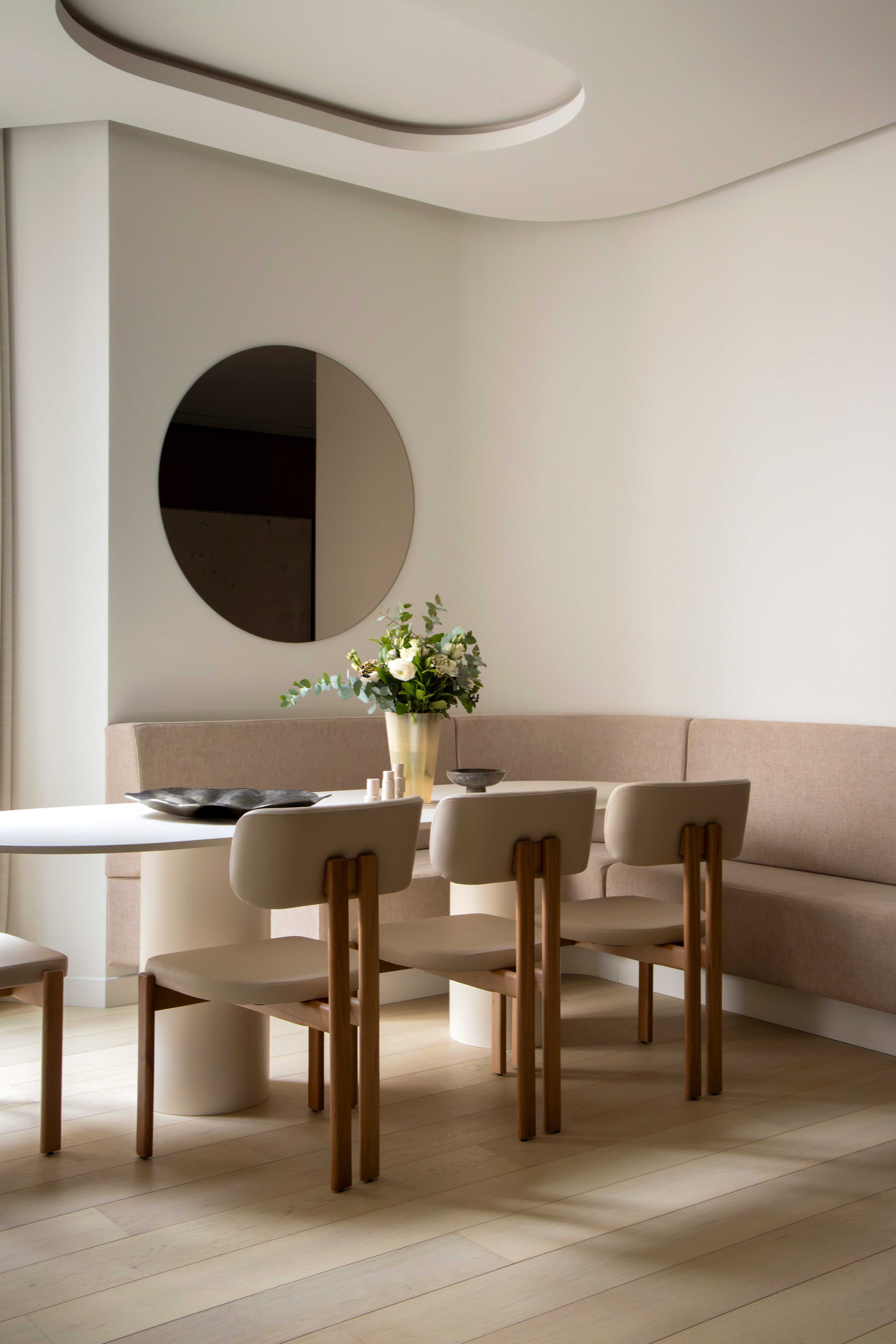 Detail de la salle a manger avec banquette courbe, chaises design, miroir rond, bouquet et plafond decoratif