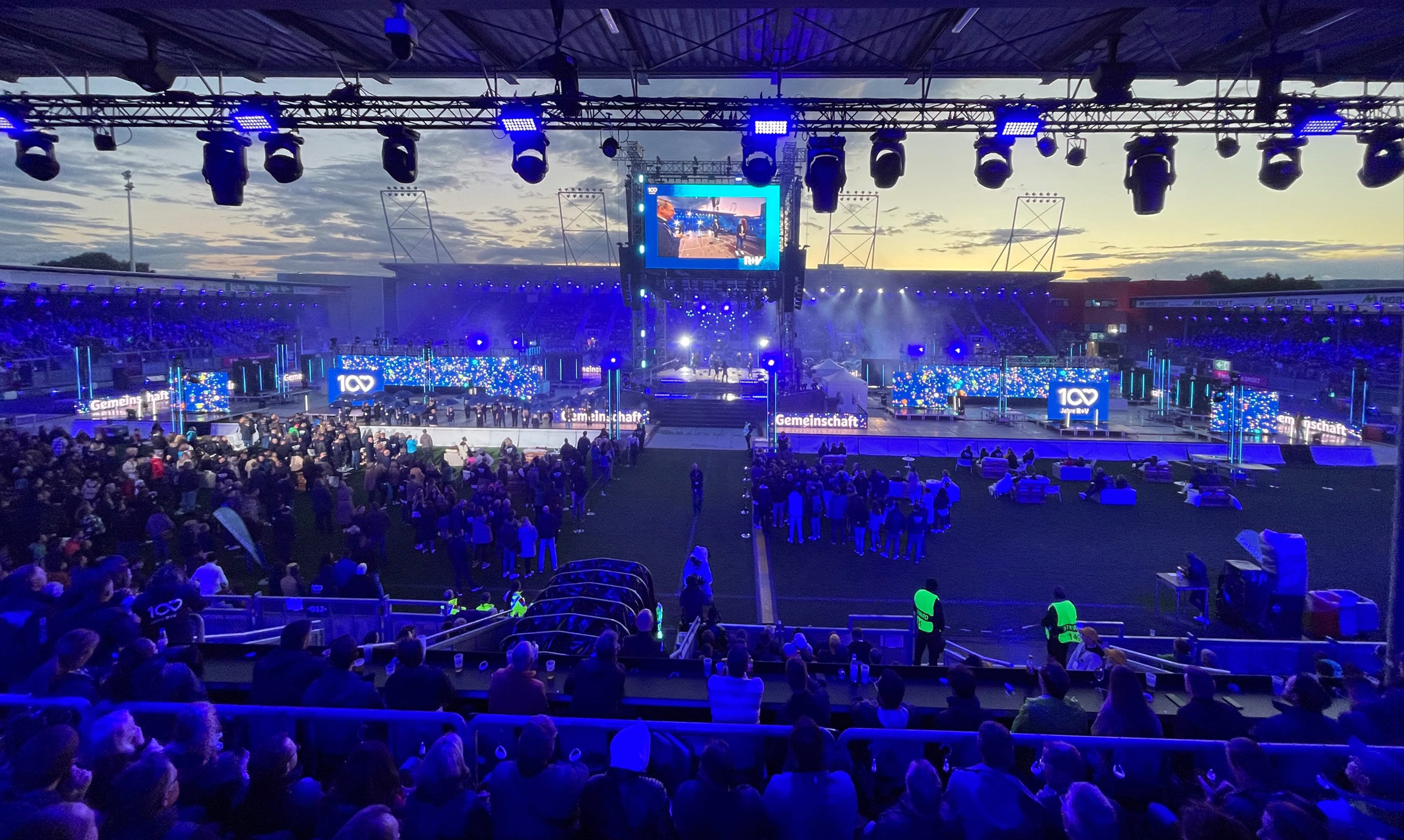 Audience attending the R+V 100 Years celebration in a stadium transformed into an immersive media environment.