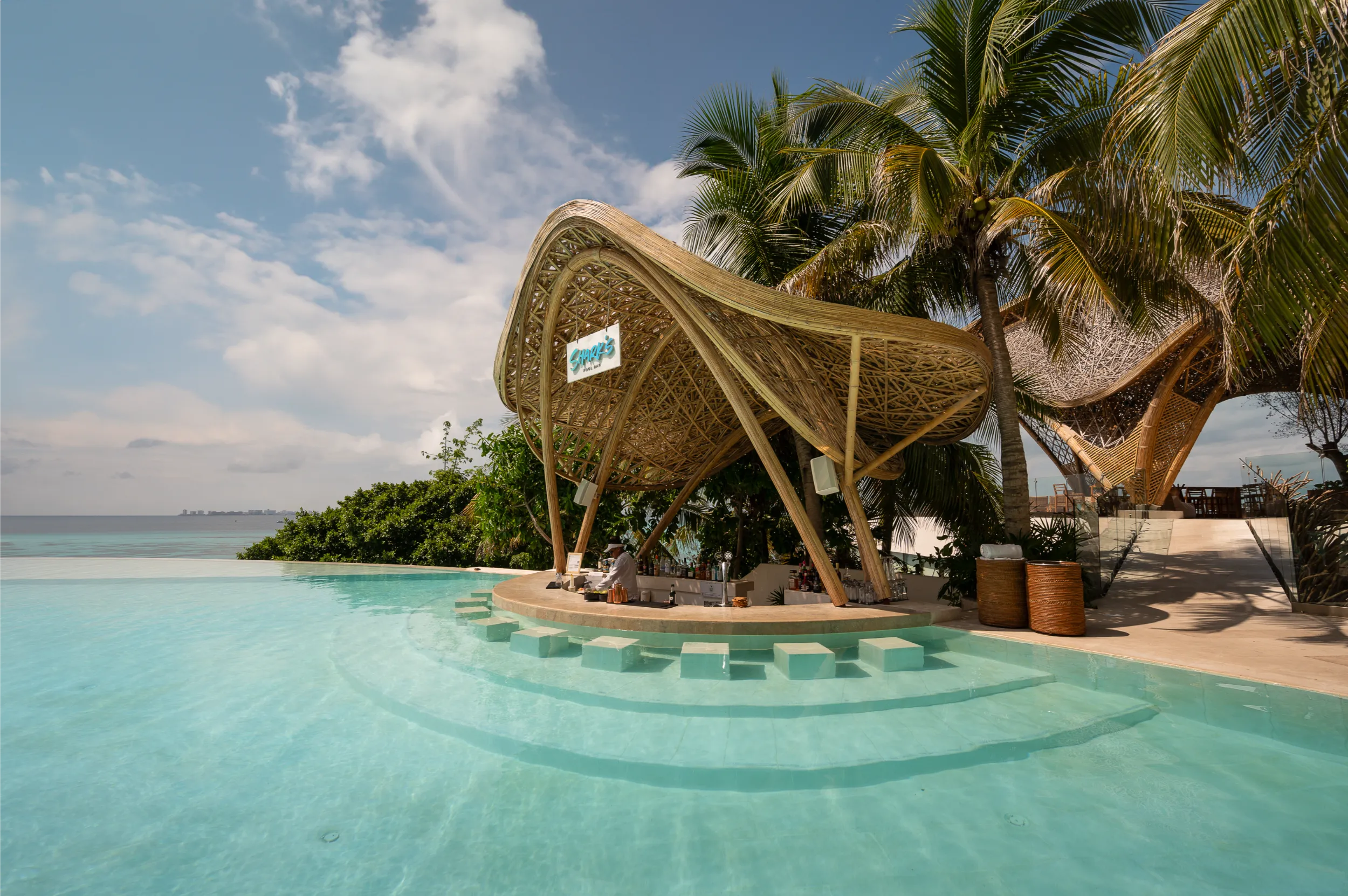 Front view of the organic bamboo 'Shark's Pool Bar' at Hyatt Impression Isla Mujeres, integrated with a luxury infinity pool and Caribbean Sea views.