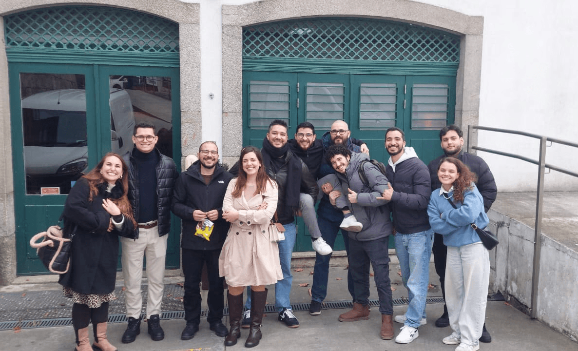 Eight man and three women smiling and posing  for a photo in front of a building.