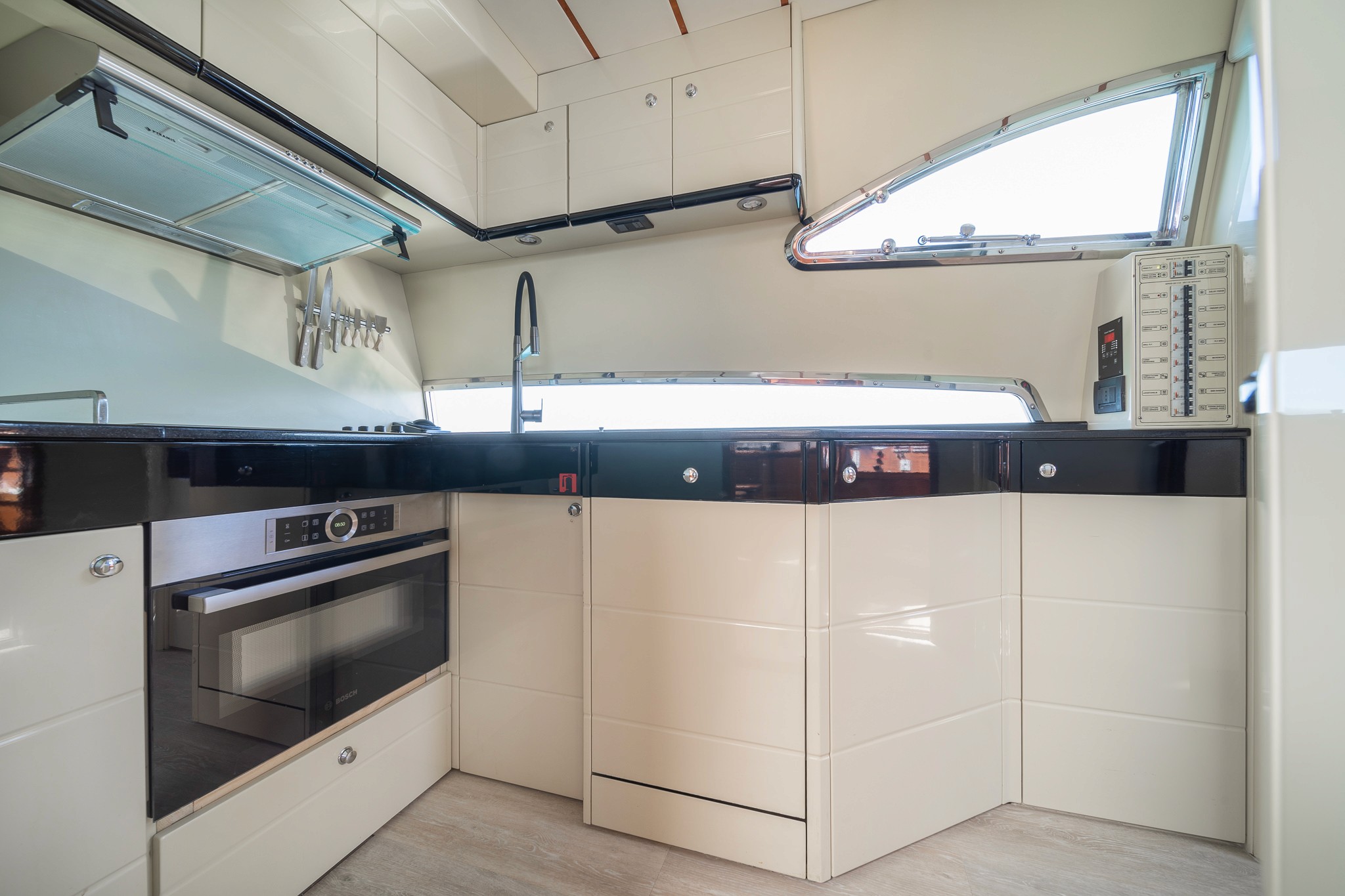 Modern yacht galley aboard Ferretti 68 with glossy white cabinetry, black countertops, and stainless steel appliances including built-in oven.