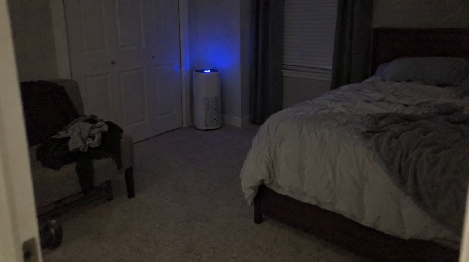 A HEPA purifier tower glowing in the corner of a dark bedroom at night.