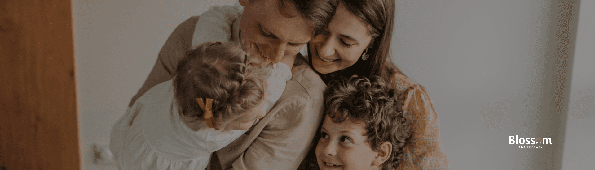 Parents hugging their children at home, symbolizing parent involvement and sibling relationships in ABA therapy, with Blossom ABA Therapy logo visible.