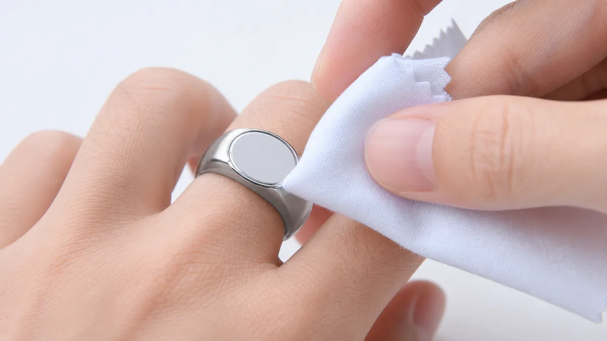 White cloth wiping the smooth sensor of a silver zikr ring while it remains on the finger