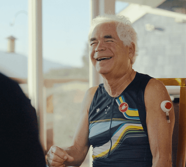 Older man exercising indoors, wearing athletic gear and a wearable health patch on his arm.
