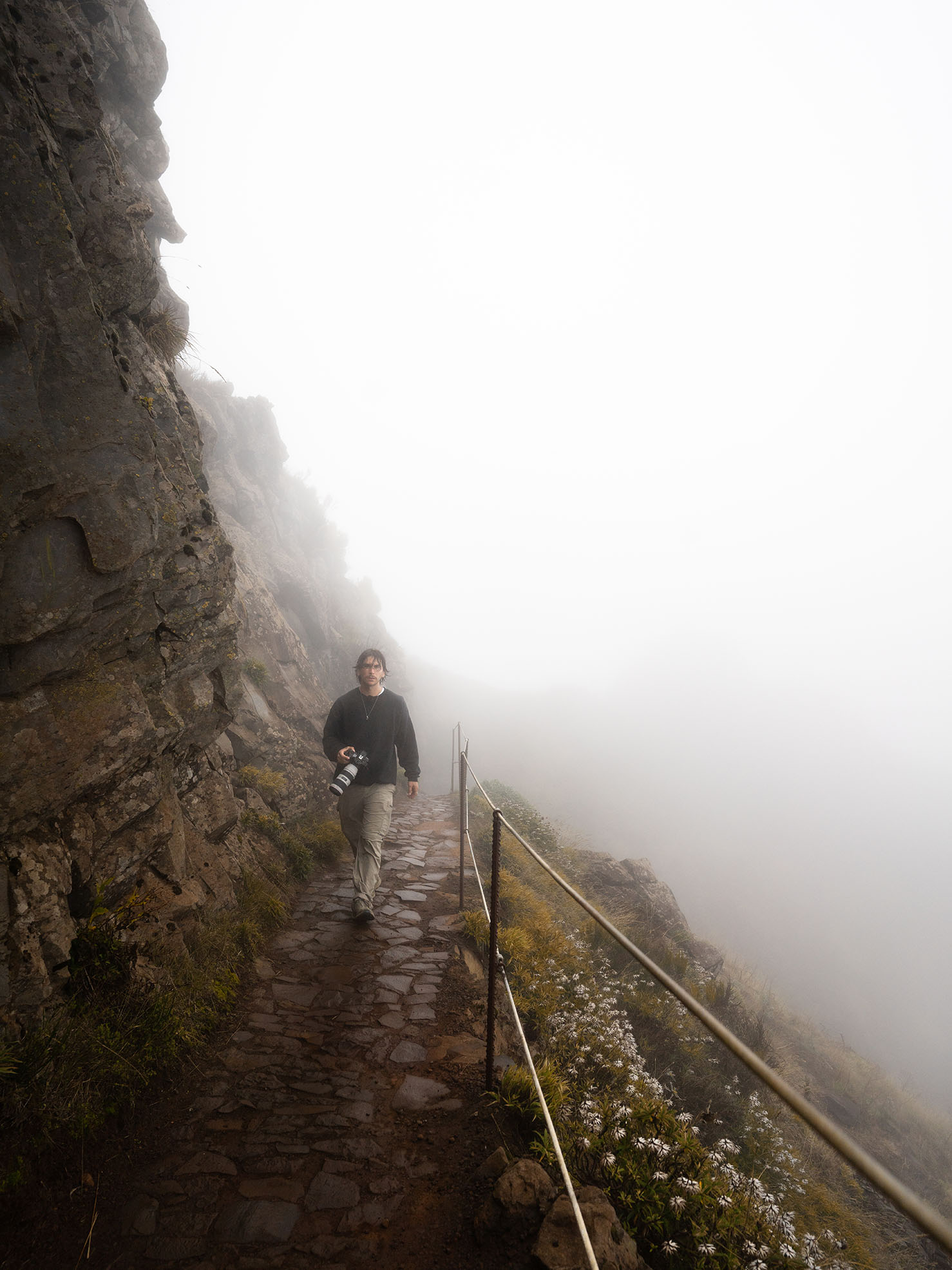 Person holding a camera on a foggy rock path.