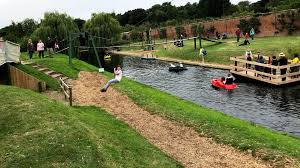 Scenic canal waterway with colorful narrowboats, wooden mooring dock and grassy towpath in rural countryside setting