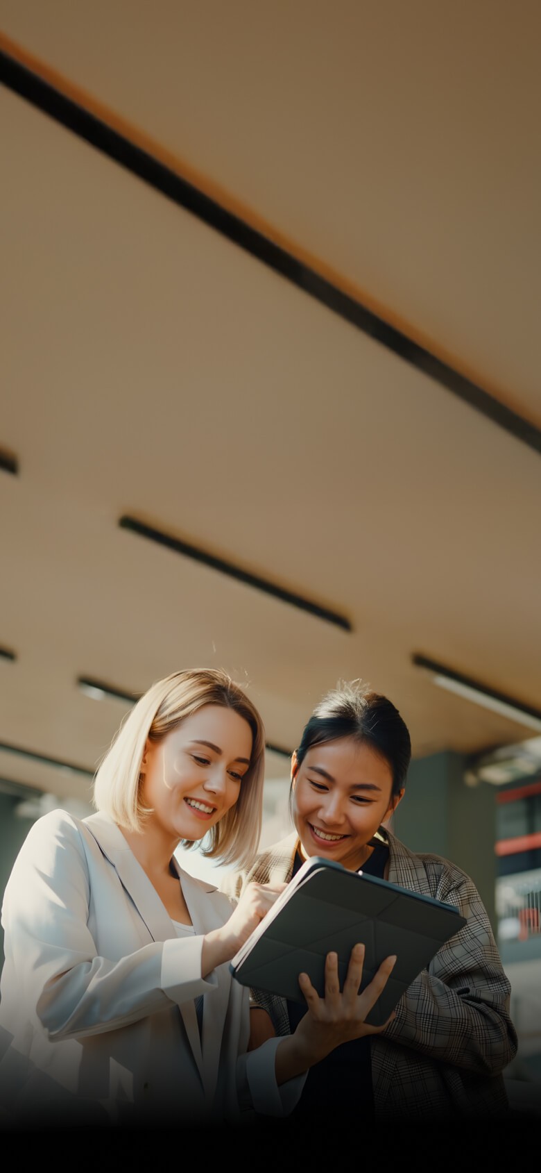 Two women in business suits looking at a tablet, likely discussing work or project details.