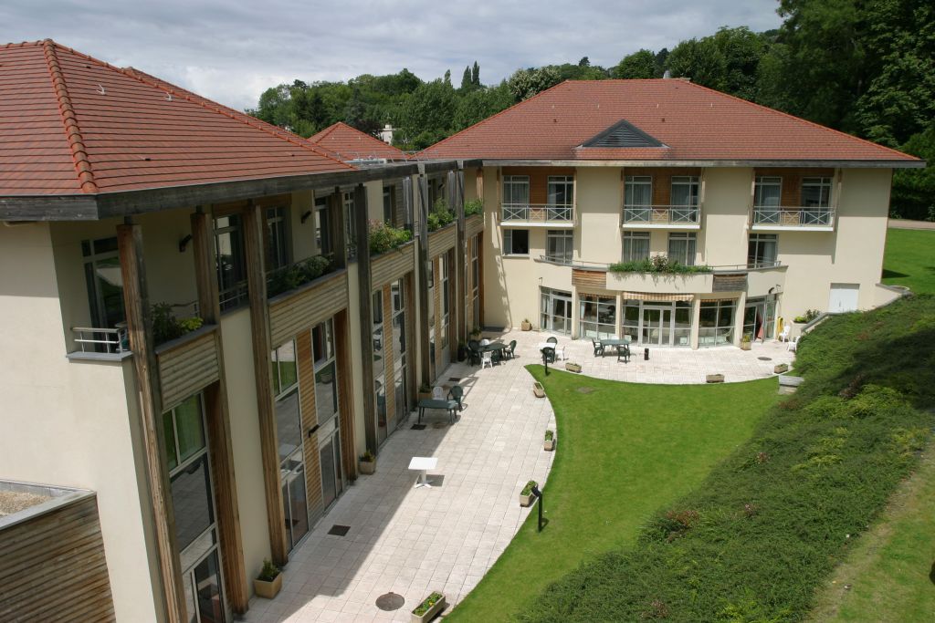 Bâtiment du centre clinique avec toit en terre cuite, murs blancs, pelouse soignée et entrée avec sentier pavé