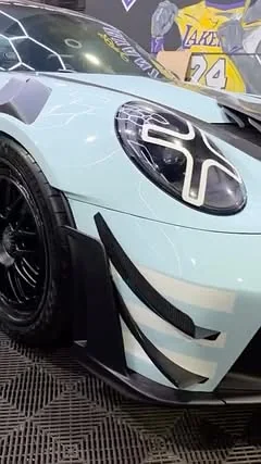 Close-up of the ice-blue GT3 RS front end showing the scale-pattern wrap graphics and carbon aero, inside the AL Custom shop