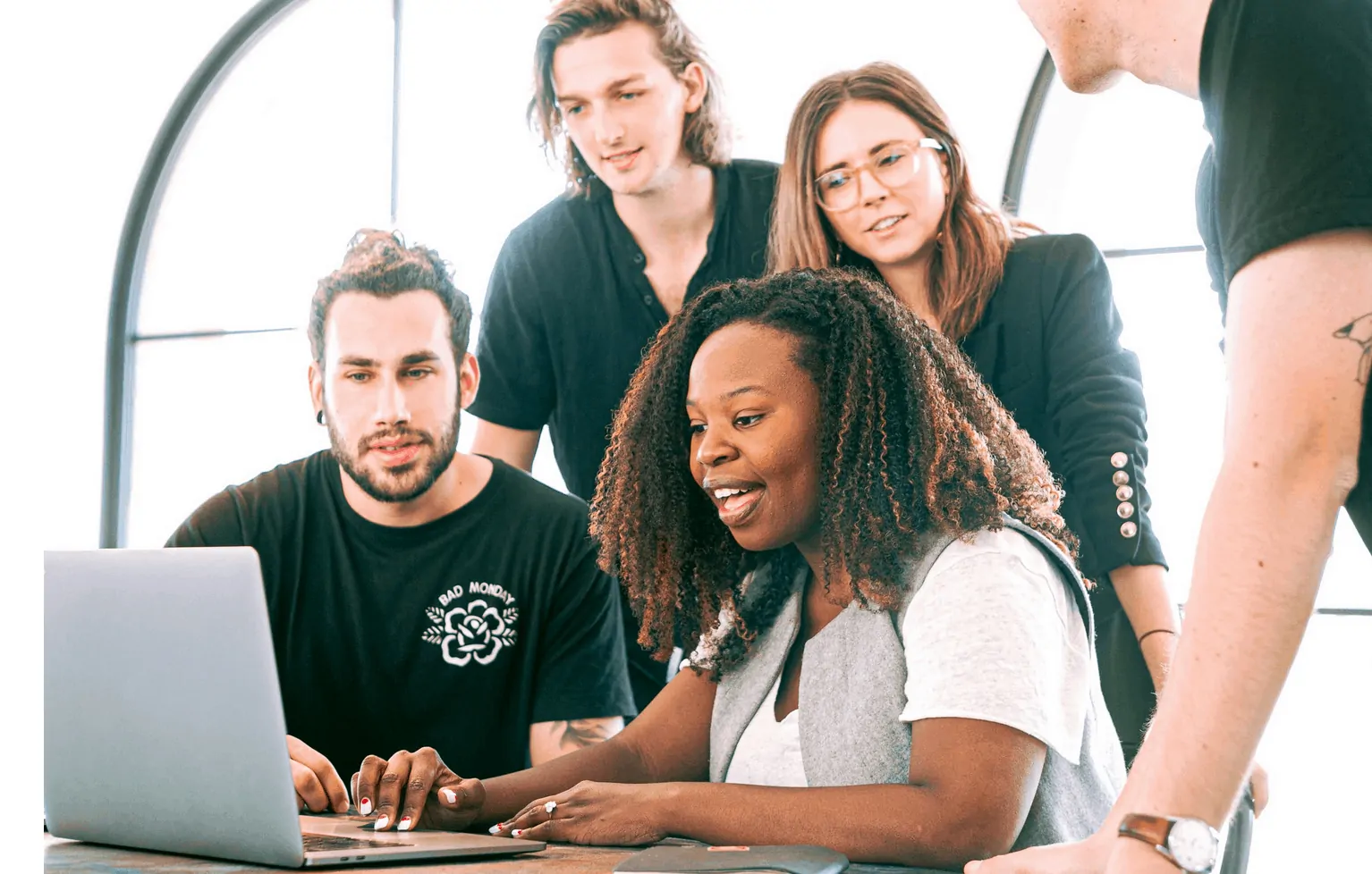  A group of five people, including one woman and four men, gathered around a laptop, discussing and collaborating on a project.