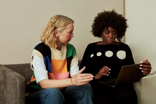 Lady with orange headphones looking at a computer screen, smiling, appearing to be on a call with someone who may be mentoring them