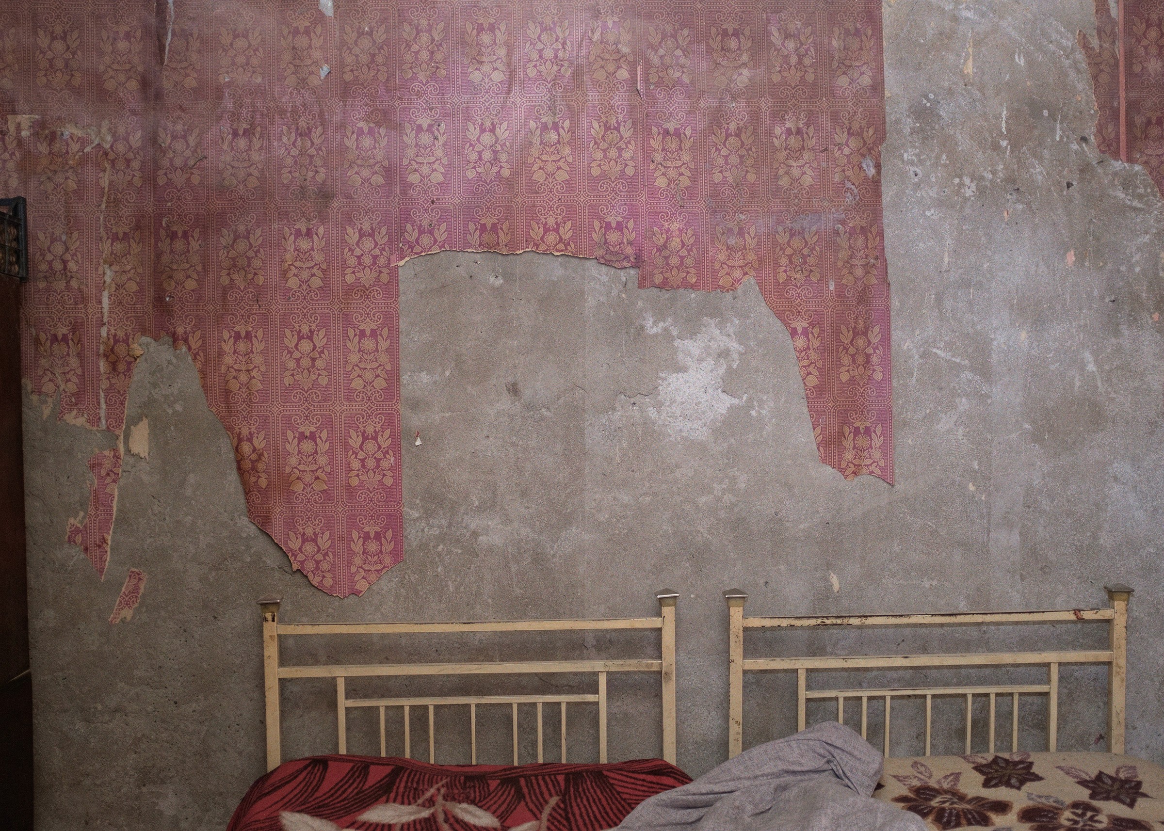 A text in Georgian about peace superimposed on a photograph of a shabby bedroom with peel-off wallpaper on the walls.