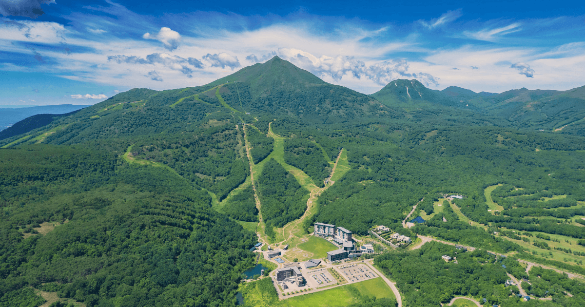 A view of a mountain resort surrounded by lush green hills under a bright blue sky.