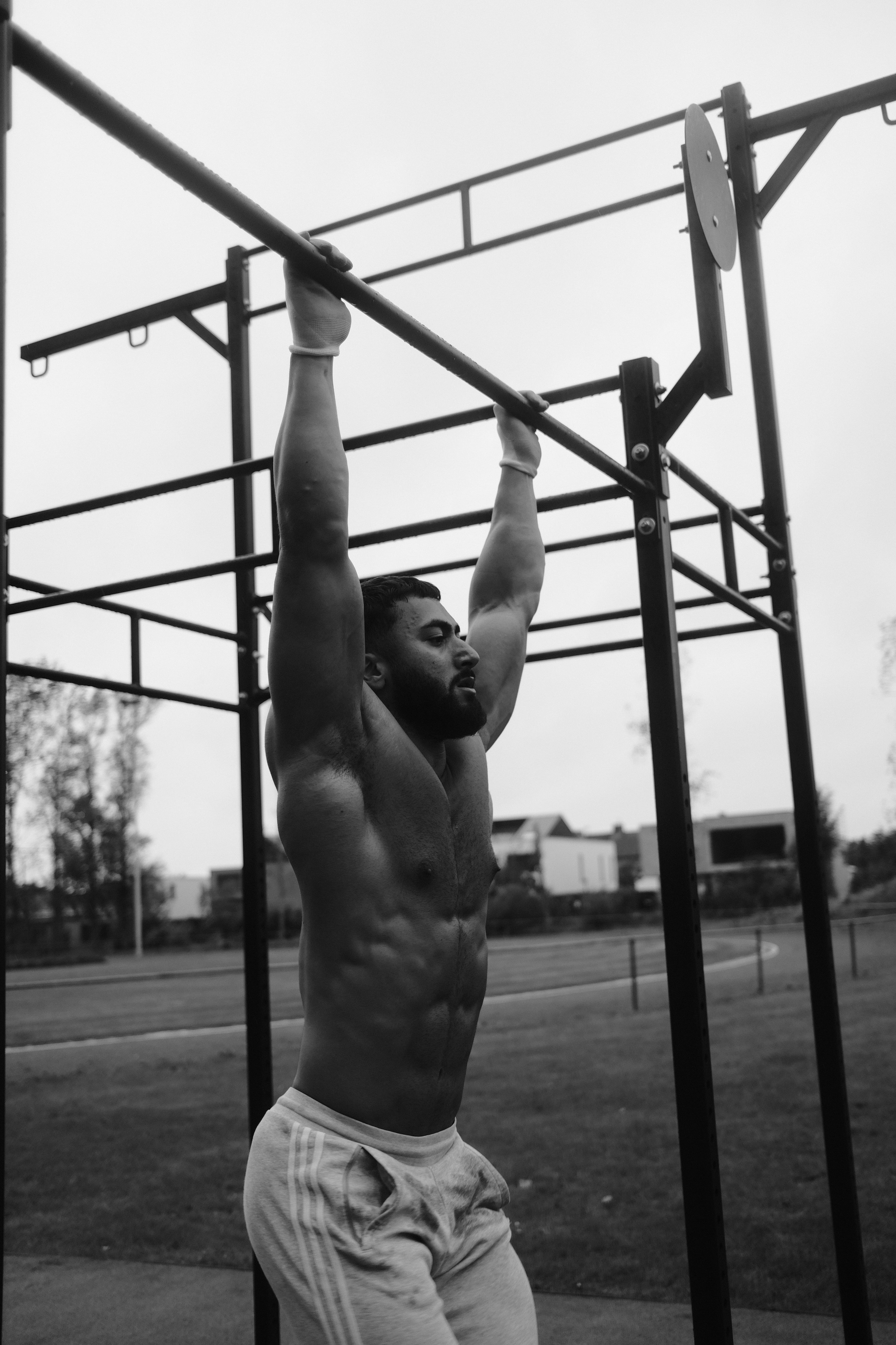 Black and white photo of FitbyElyas doing a pull up on outdoor workout bars.