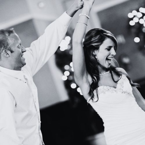 A newlywed couple and their guests dancing and celebrating at the wedding reception, the room lit up with colorful lighting and filled with a sense of happiness and energy.