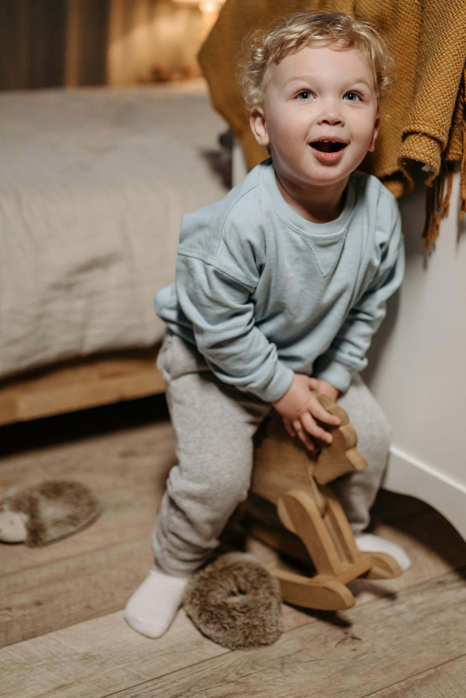 A cheerful toddler sits on a colorful wooden toy, smiling and enjoying playtime in a bright, cozy room