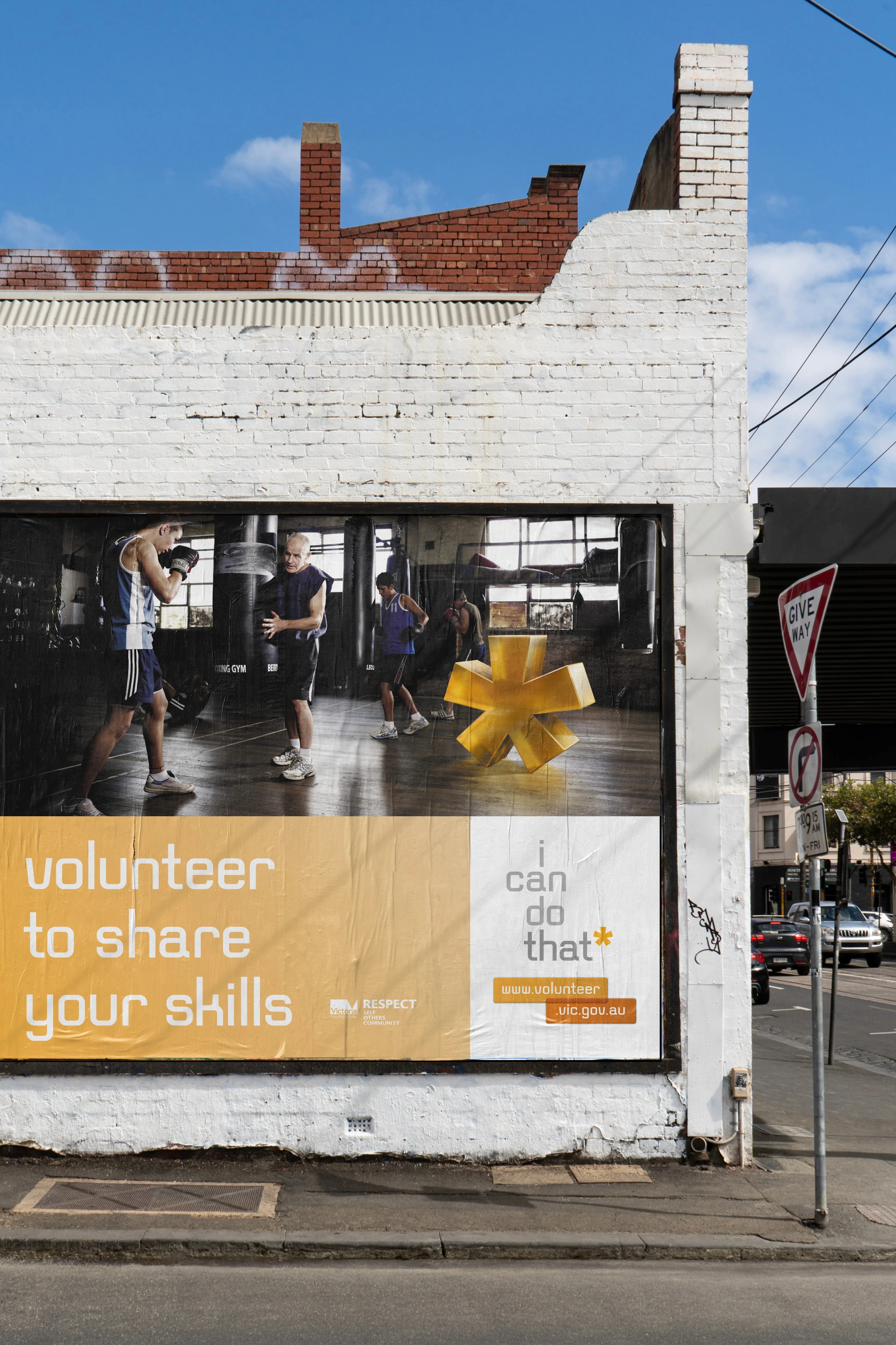 Billboard on a white brick wall: 'volunteer to share your skills', with boxing trainers and a yellow asterisk