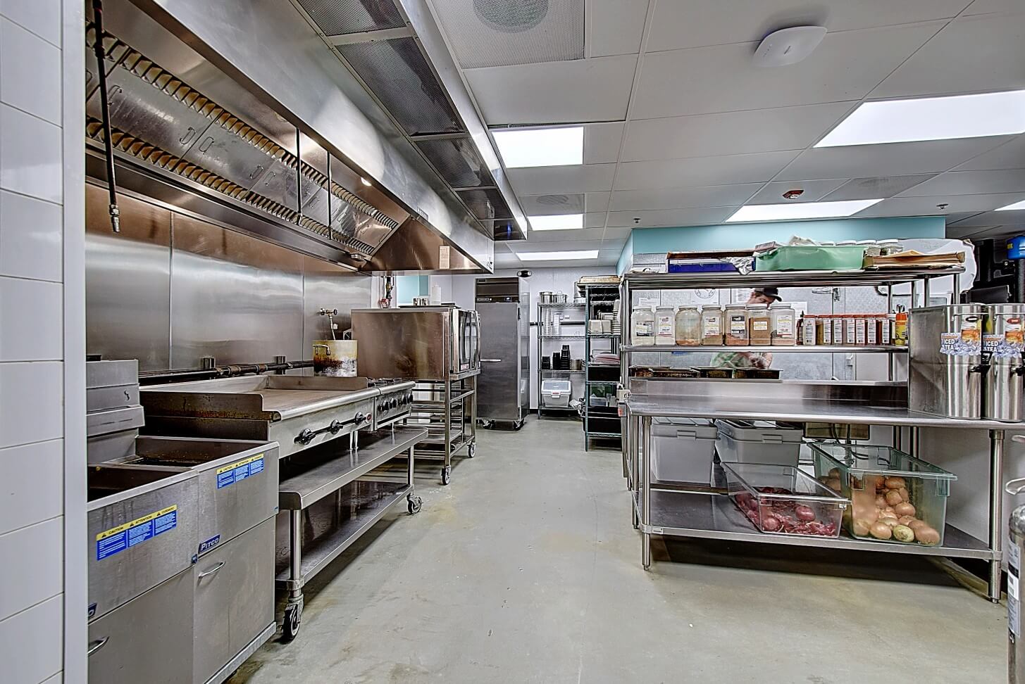 A modern kitchen interior with stainless steel shelves and equipment, well-lit, and organized for food preparation.